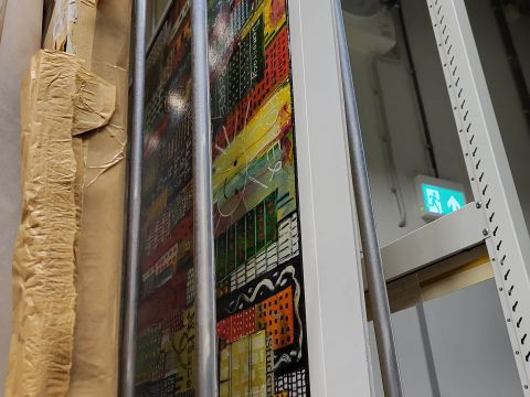 A metal rack holding a painting donated from Hong Kong. The painting was created during the Democratic Protests and depicts city life during this time. Photo Credit: Enrico Joaquin Lapuz 