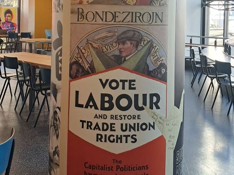 A collection of trade union posters in the IISH cafeteria. In the center, the poster calls to "Vote Labour and Restore Trade Union Rights". On the top-left, the poster says De Moderne Vakbeweging Eischt Een Vakantieregeling, which means "The Modern Trade Union Movement Demands a Holiday Scheme" in Dutch; Photo Credit: Meera Venkatachalam (2024)