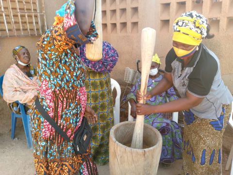 Three Burkinabe women surrounding a large mortar and pestle, pounding soumbala seeds.; Credit: Jocelyne Vokouma