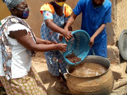 Three Burkinabe women around a boiling pot of water, cooking softened soumbala spice seeds.; Credit: Jocelyne Vokouma